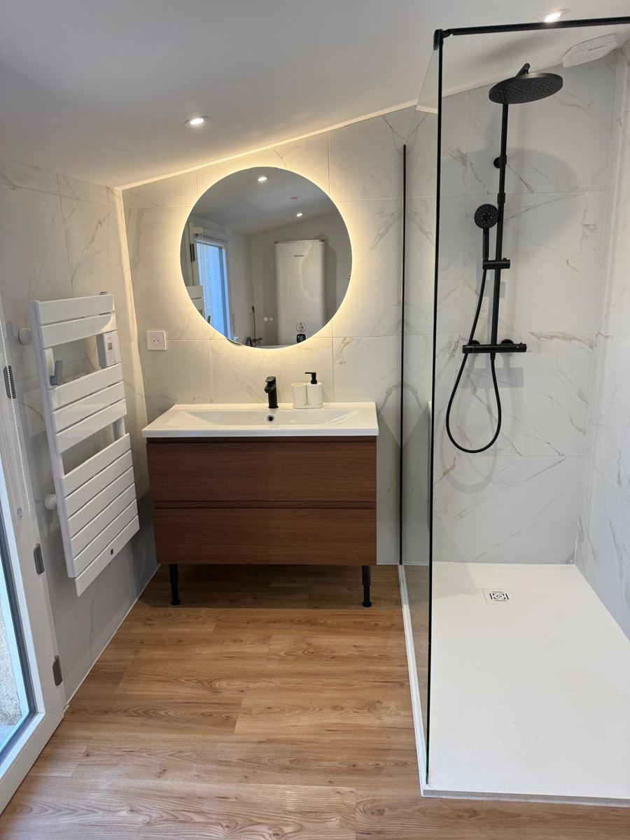Après : salle de bain rénovée avec douche à l'italienne, meuble vasque en bois et miroir rond éclairé
