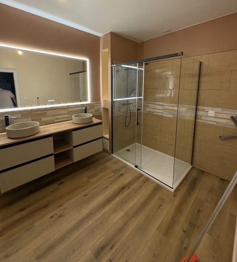 Salle de bain rénovée par LSC : double vasque, miroir LED, douche vitrée et sol effet bois